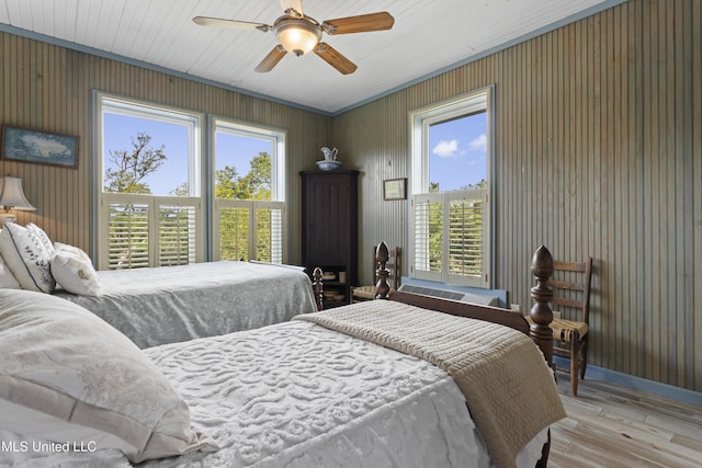 bedroom with multiple windows, wood walls, wood finished floors, and a ceiling fan