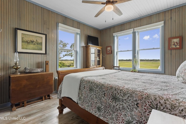 bedroom with a ceiling fan, wooden walls, and light wood-type flooring