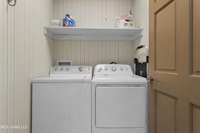 clothes washing area with laundry area, wood walls, and washing machine and dryer