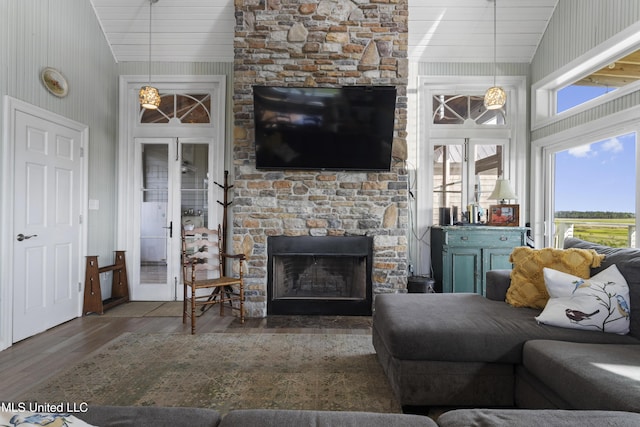 living area featuring lofted ceiling, a wealth of natural light, a stone fireplace, and wood finished floors