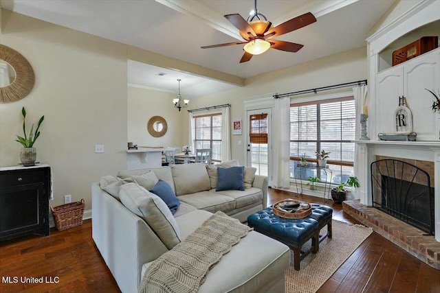 living area with ceiling fan with notable chandelier, dark wood-type flooring, a fireplace, and baseboards