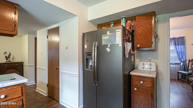 kitchen with brown cabinetry, dark wood-style flooring, light countertops, and stainless steel fridge