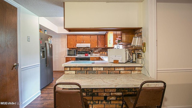 kitchen with stainless steel fridge, brown cabinets, dark wood-style flooring, electric stove, and under cabinet range hood