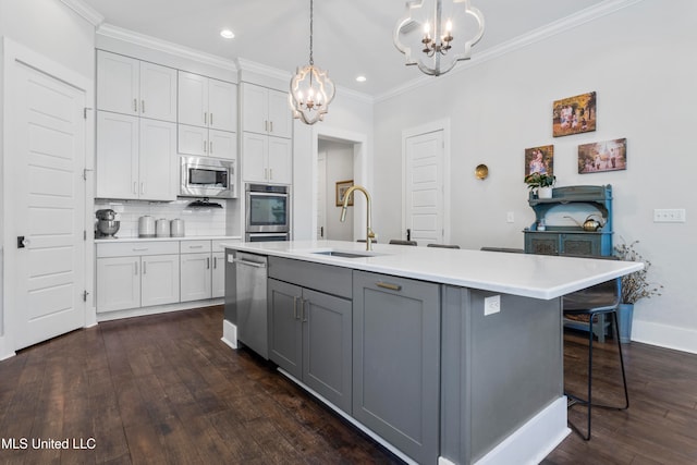 kitchen featuring dark hardwood / wood-style flooring, stainless steel appliances, sink, hanging light fixtures, and an island with sink