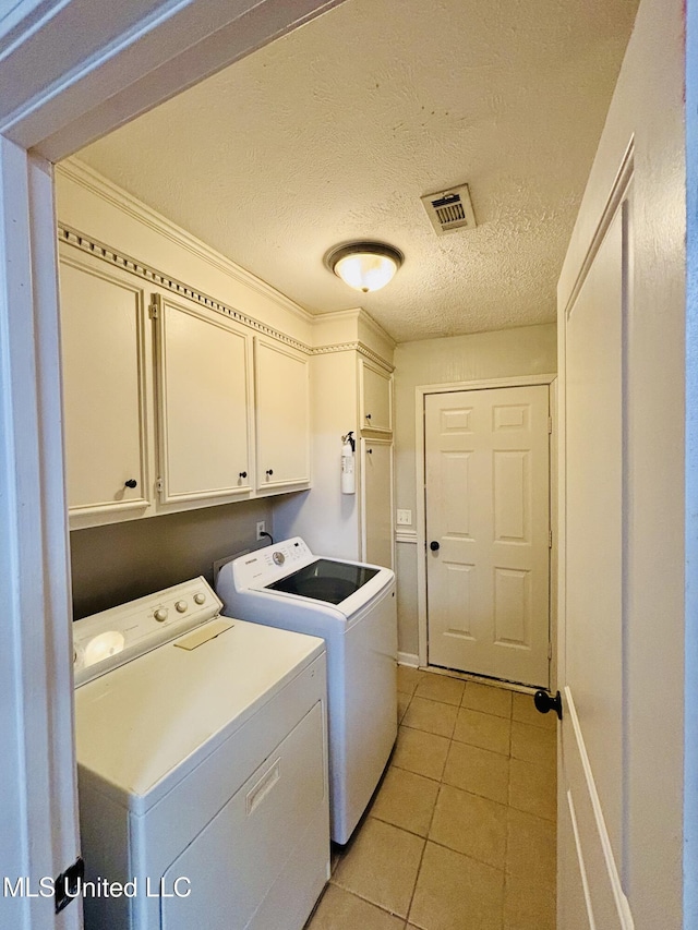 clothes washing area with washing machine and dryer, a textured ceiling, light tile patterned floors, and cabinets