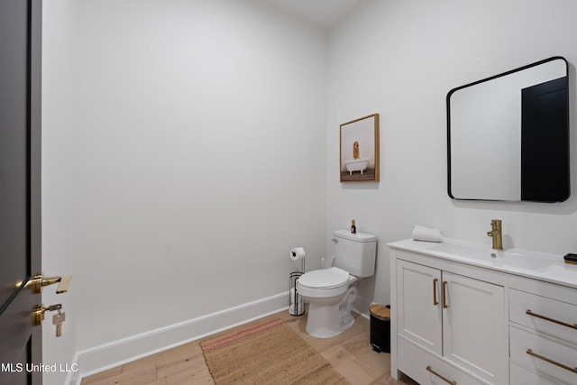 half bath with toilet, wood finished floors, vanity, and baseboards