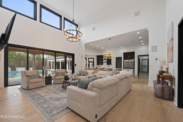 living room featuring light wood-type flooring, a towering ceiling, visible vents, and a notable chandelier