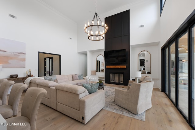 living area featuring light wood-type flooring, a large fireplace, visible vents, and ornamental molding