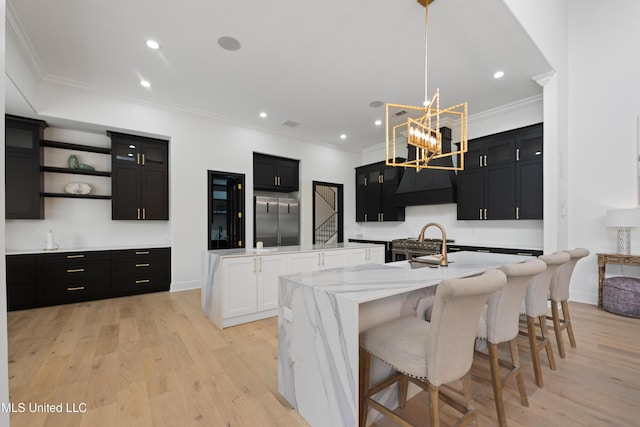 kitchen with high quality appliances, ornamental molding, dark cabinetry, a large island with sink, and light wood-type flooring