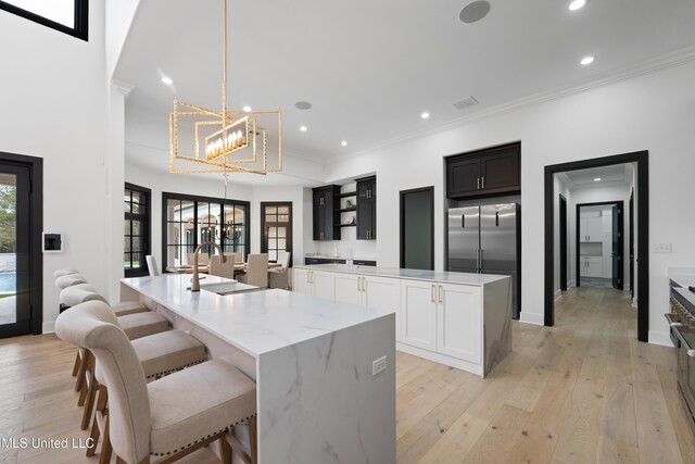 kitchen with a chandelier, a spacious island, ornamental molding, open shelves, and light wood finished floors