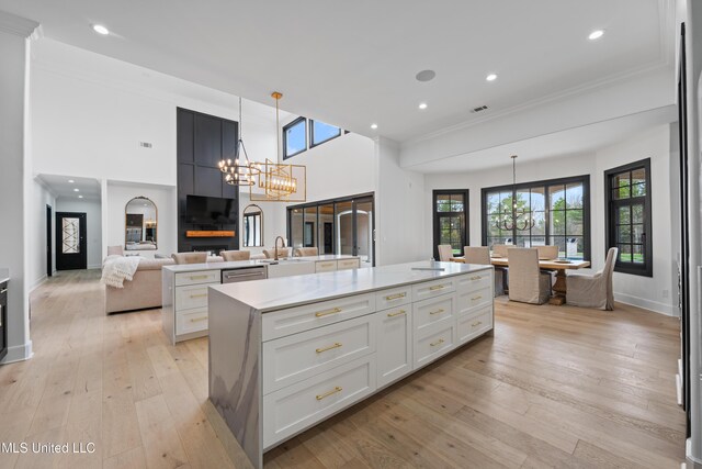 kitchen with a sink, light wood-style floors, a large island, decorative light fixtures, and an inviting chandelier