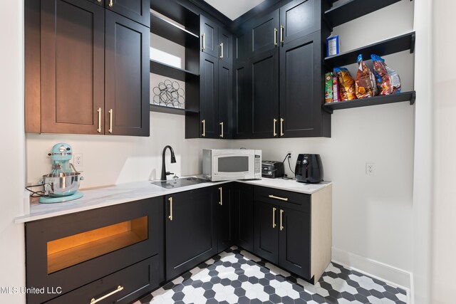 kitchen with open shelves, light countertops, white microwave, a sink, and dark cabinetry