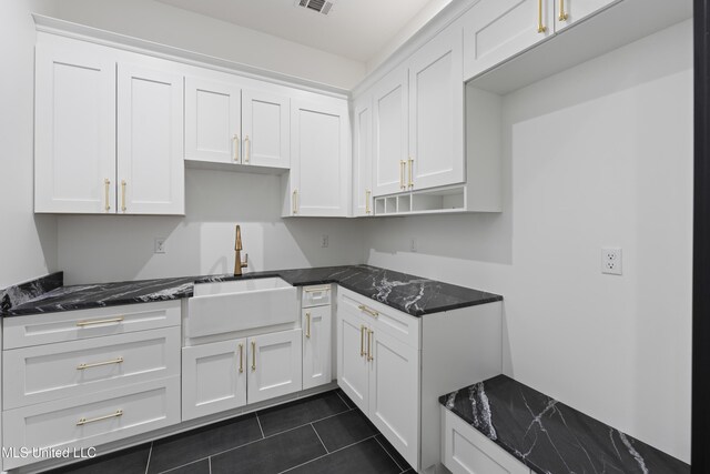 kitchen with visible vents, dark stone counters, white cabinets, dark tile patterned flooring, and a sink