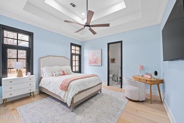 bedroom featuring multiple windows, a raised ceiling, visible vents, and light wood-style floors