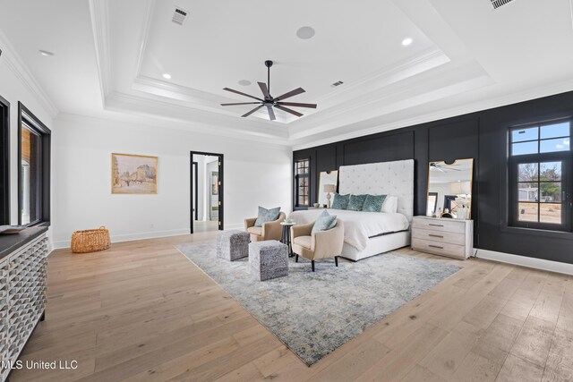 bedroom with visible vents, baseboards, light wood-style floors, a raised ceiling, and crown molding