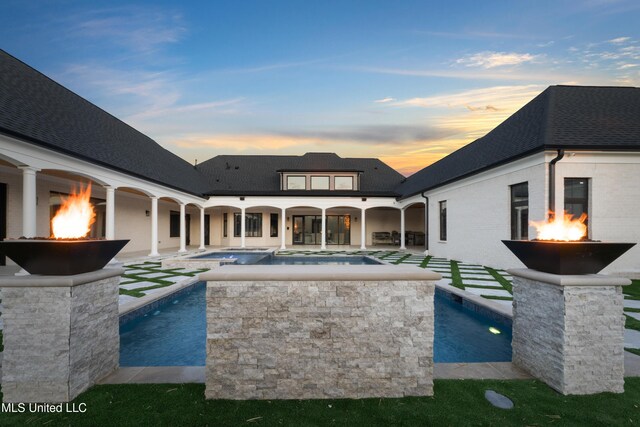 back of property with an outdoor pool, a patio, roof with shingles, an in ground hot tub, and brick siding