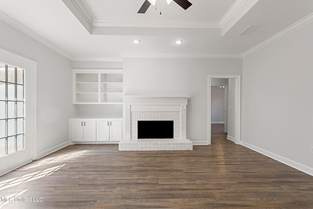 unfurnished living room with dark hardwood / wood-style floors, crown molding, a brick fireplace, a raised ceiling, and ceiling fan