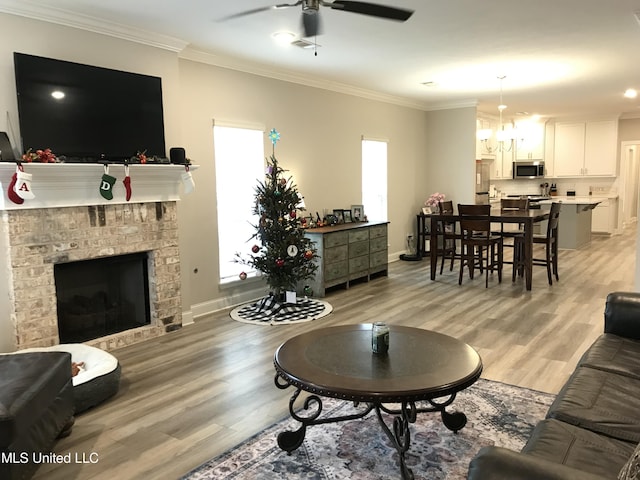 living room featuring ceiling fan, light hardwood / wood-style floors, crown molding, and a brick fireplace