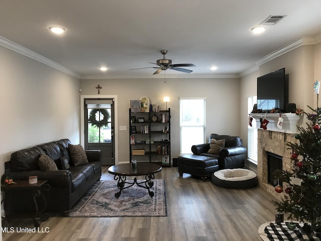 living room with a stone fireplace, crown molding, ceiling fan, and hardwood / wood-style flooring