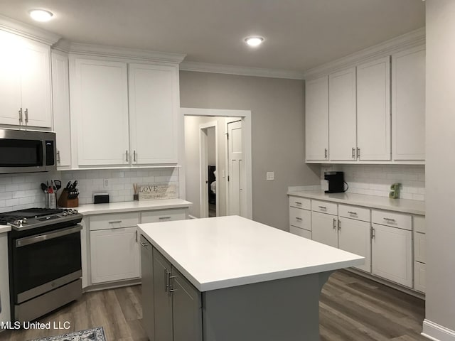 kitchen with appliances with stainless steel finishes, dark wood-type flooring, crown molding, white cabinets, and a kitchen island