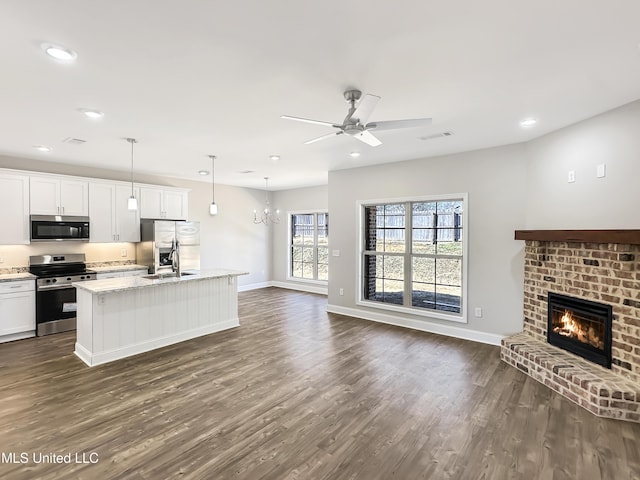 kitchen featuring an island with sink, appliances with stainless steel finishes, white cabinets, and decorative light fixtures