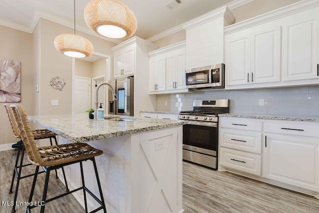 kitchen featuring white cabinetry, hanging light fixtures, stainless steel appliances, a kitchen breakfast bar, and a kitchen island with sink