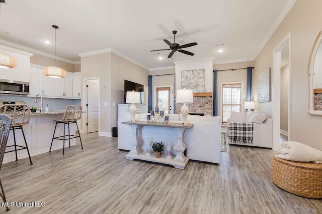 living room featuring crown molding, light hardwood / wood-style flooring, ceiling fan, and sink