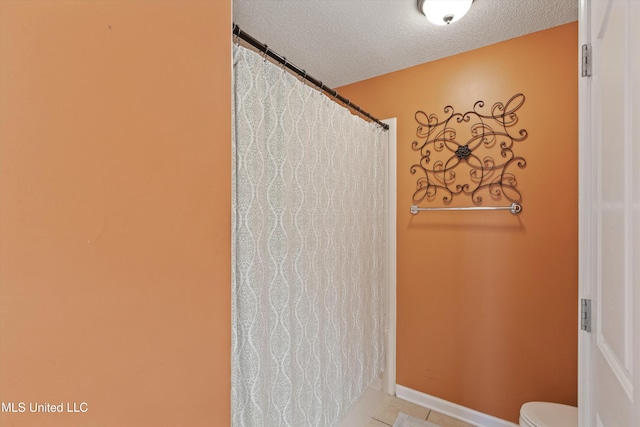 bathroom featuring a shower with shower curtain, baseboards, a textured ceiling, and toilet