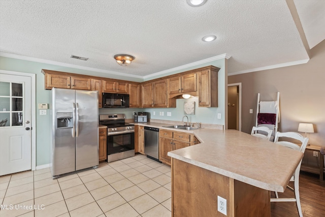 kitchen with appliances with stainless steel finishes, brown cabinetry, a sink, and a peninsula