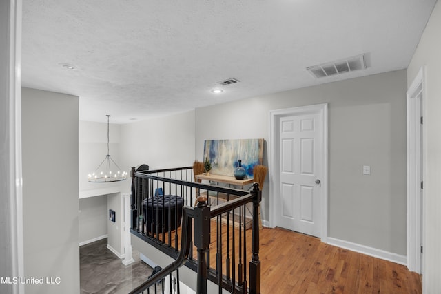 hallway with a notable chandelier, a textured ceiling, and wood-type flooring