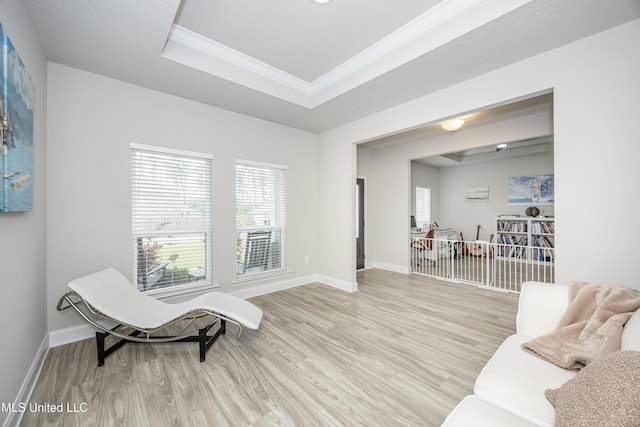 living area with light wood-style floors, crown molding, a tray ceiling, and baseboards