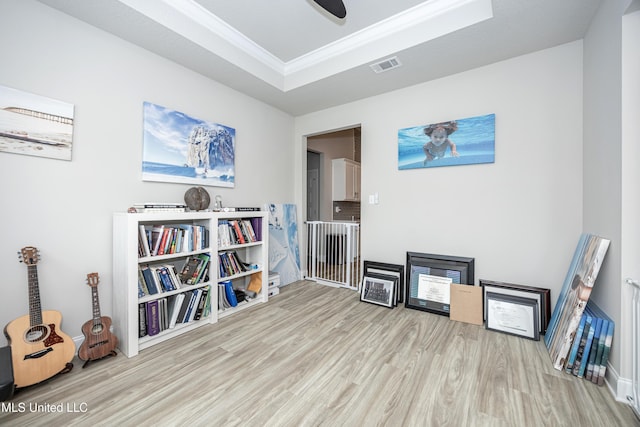 sitting room with a raised ceiling, wood finished floors, crown molding, and visible vents