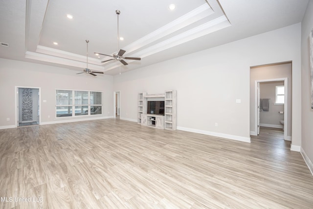 unfurnished living room with crown molding, a raised ceiling, ceiling fan, baseboards, and light wood finished floors