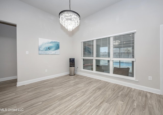 spare room featuring baseboards, a chandelier, and light wood-type flooring