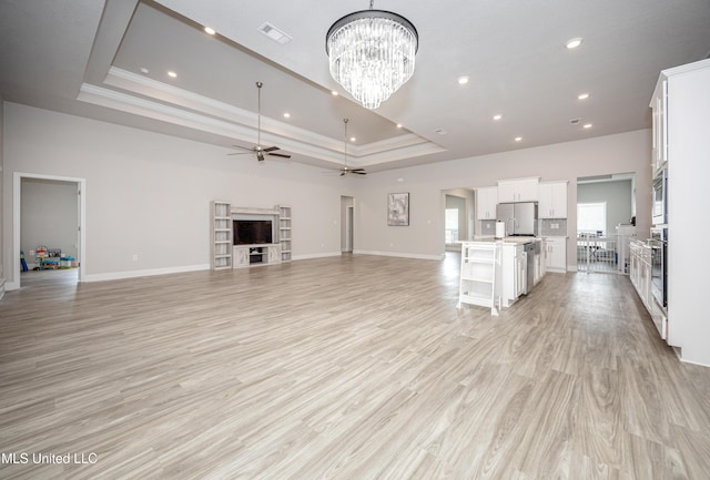 unfurnished living room featuring recessed lighting, a tray ceiling, visible vents, baseboards, and ceiling fan with notable chandelier