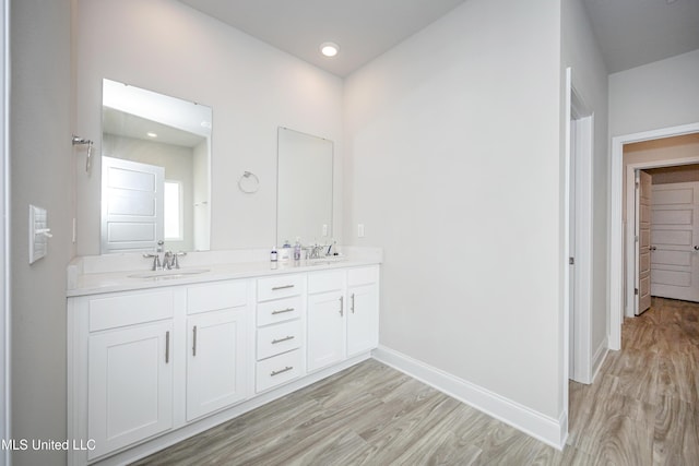 bathroom with baseboards, wood finished floors, double vanity, and a sink