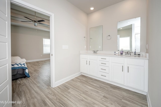 bathroom featuring wood finished floors, double vanity, ceiling fan, a sink, and baseboards