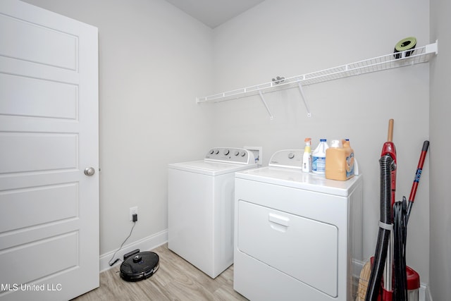 clothes washing area featuring washing machine and dryer, light wood finished floors, laundry area, and baseboards