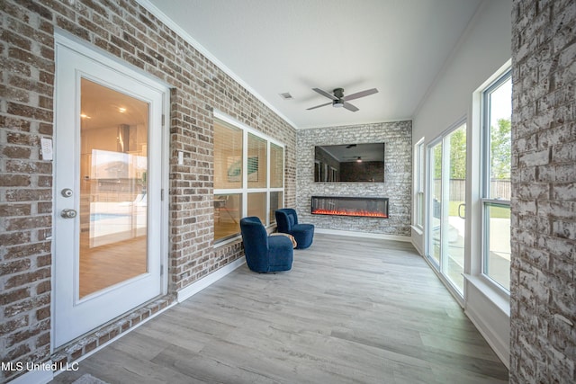 unfurnished sunroom with wood finished floors, brick wall, ornamental molding, baseboards, and visible vents