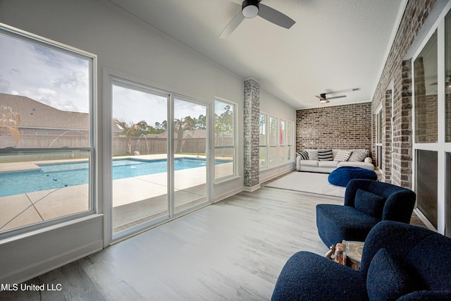 sunroom with lofted ceiling, wood finished floors, brick wall, and a ceiling fan