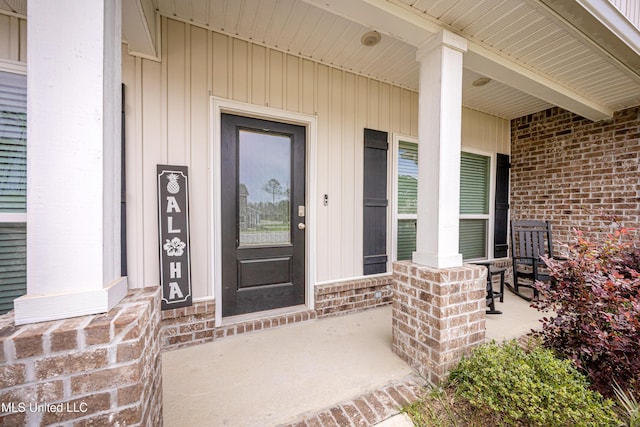 property entrance featuring covered porch, board and batten siding, and brick siding