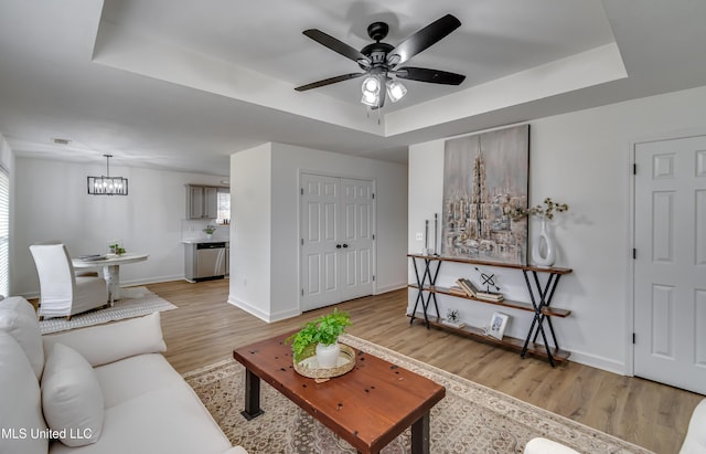 living area with a tray ceiling, visible vents, ceiling fan, light wood-type flooring, and baseboards