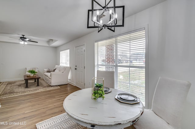 dining area featuring a tray ceiling, wood finished floors, and ceiling fan with notable chandelier