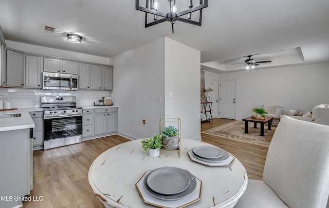 dining room featuring light wood-style flooring, visible vents, a raised ceiling, and ceiling fan with notable chandelier