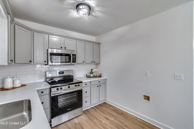 kitchen with gray cabinetry, light countertops, appliances with stainless steel finishes, decorative backsplash, and light wood finished floors