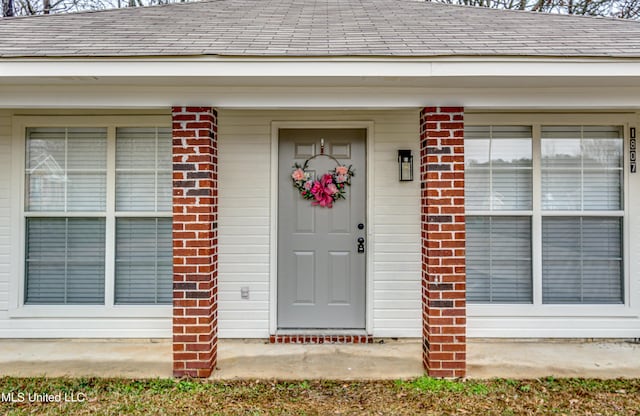 doorway to property featuring a shingled roof and brick siding