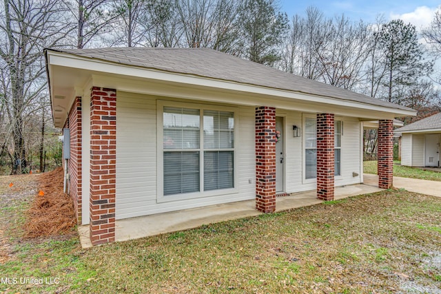 view of front facade with roof with shingles, a front yard, and brick siding