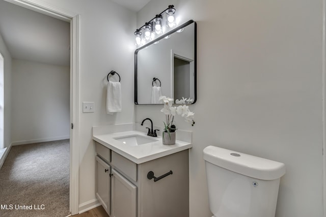 half bathroom featuring toilet, baseboards, and vanity