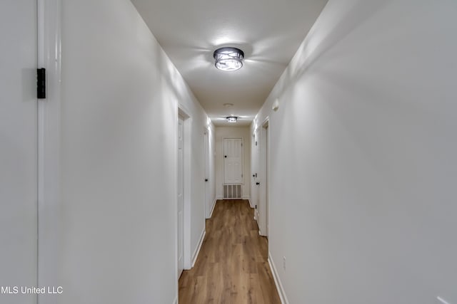 hallway featuring baseboards, visible vents, and light wood finished floors