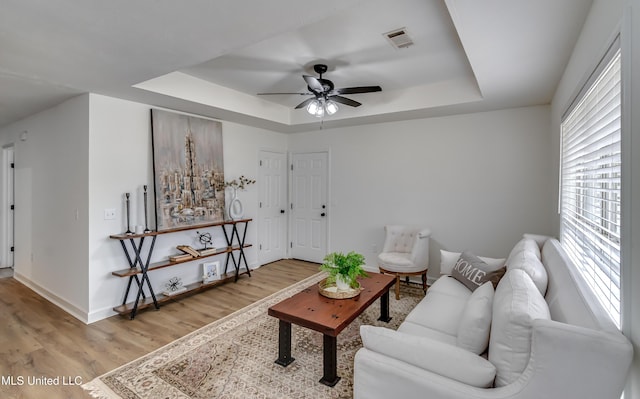 living area with a tray ceiling, visible vents, light wood-style floors, a ceiling fan, and baseboards